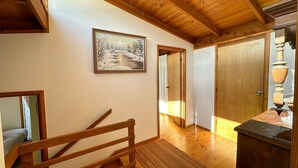 A wooden staircase leading to a bedroom, a wooden door, and a painting of a snowy landscape on the wall.