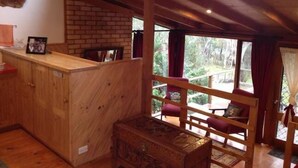A rustic wooden cabin with a loft bedroom, a brick fireplace, and a view of the surrounding forest.