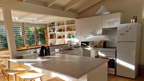 A modern kitchen with a large island, white cabinetry, and a view of greenery through the window. - Lark Cottage - relaxing retreat (Burrawang)