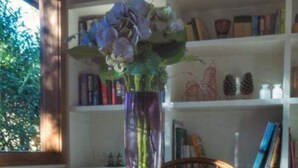 A dining table with a plate of food, a vase with flowers, and a bookshelf in the background. - Lark Cottage - relaxing retreat (Burrawang)