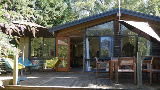 A wooden cabin with large glass windows, a deck with outdoor furniture, and a covered patio area. - Lark Cottage - relaxing retreat (Burrawang)