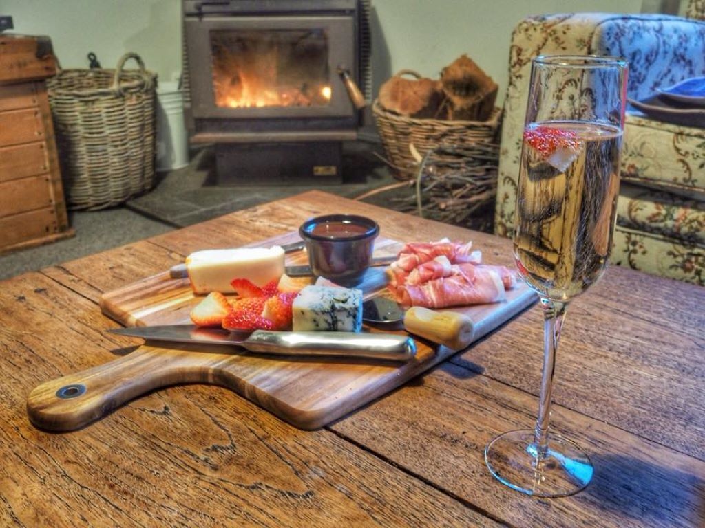 A wooden table with a cheese board, a glass of wine, and a cutting board with various cheeses and meats.