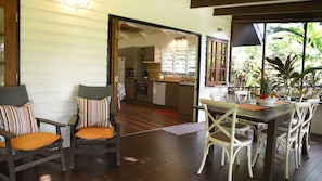 A dining area with wooden flooring, a table with chairs, and a view of the kitchen through an open doorway.