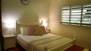 A bedroom with a bed, bedside lamps, a nightstand, a window with blinds, and a wall clock.