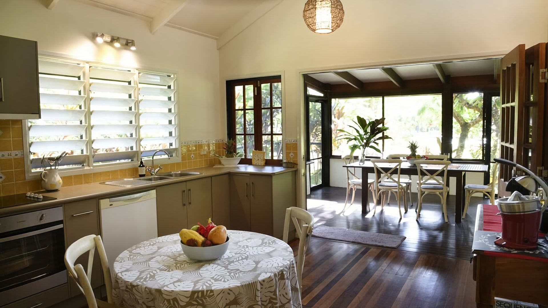 A kitchen with a dining area, a wooden floor, and a view through the open door.