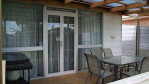 En overdækket terrasse med bord og stole, grill og en skydedør af glas.