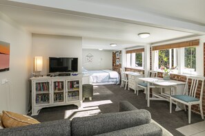 Ein gemütliches Zimmer mit einem Bett, einem Fernseher, einem Bücherregal und einem Essbereich mit Tisch und Stühlen.
