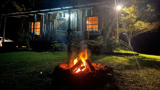 A rustic cabin with a fire pit in the foreground, surrounded by a grassy yard and trees. - Willow Cottage @ Hidden Valley Retreat Cottages (Grose Vale)