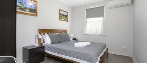 A neatly arranged bedroom with a bed, bedside tables, a chair, and two framed pictures on the wall.