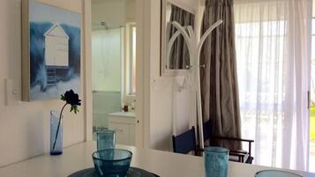 Un coin repas avec une table blanche, de la verrerie bleue et un tableau représentant une maison.