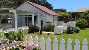 A single-story house with a red roof, white exterior, and a covered porch. - Garden Studio ~ Coromandel Apartments (Coromandel Township)