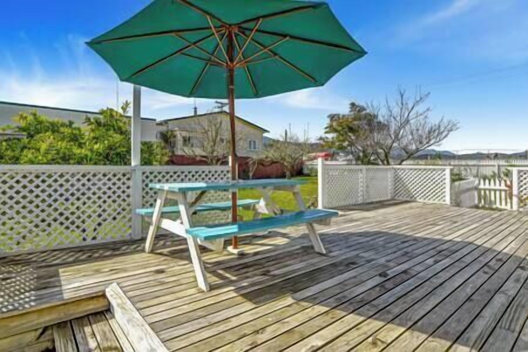 Une terrasse en bois avec une table de pique-nique et un parasol vert.