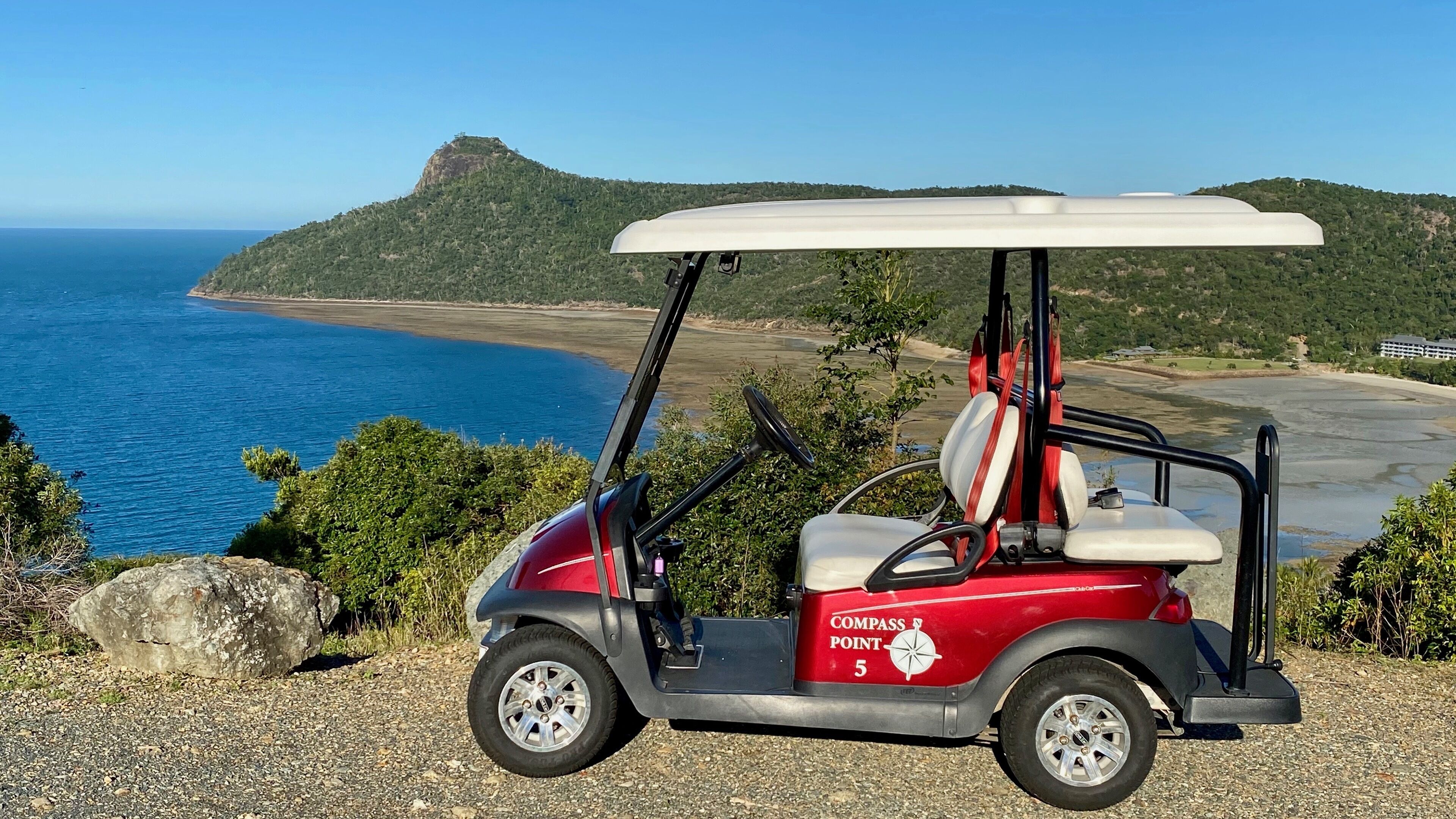 A golf cart with a canopy parked on a gravel path with a view of a coastal landscape.
