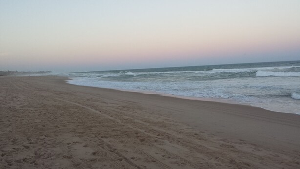 Una amplia playa de arena con huellas visibles que se dirigen hacia el océano.