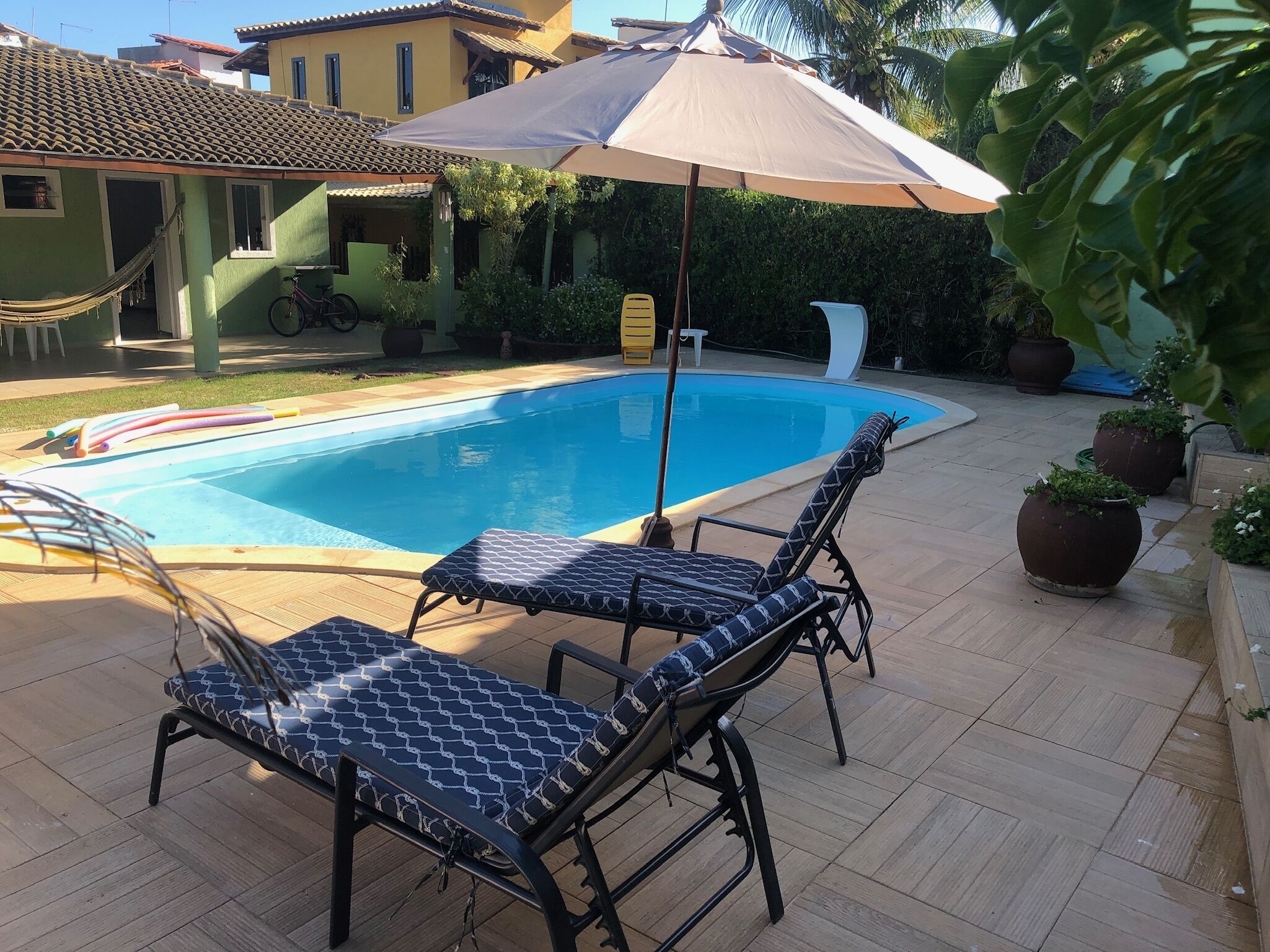 Zwembad met ligbedden en een parasol, omgeven door potplanten en een betegeld terras.