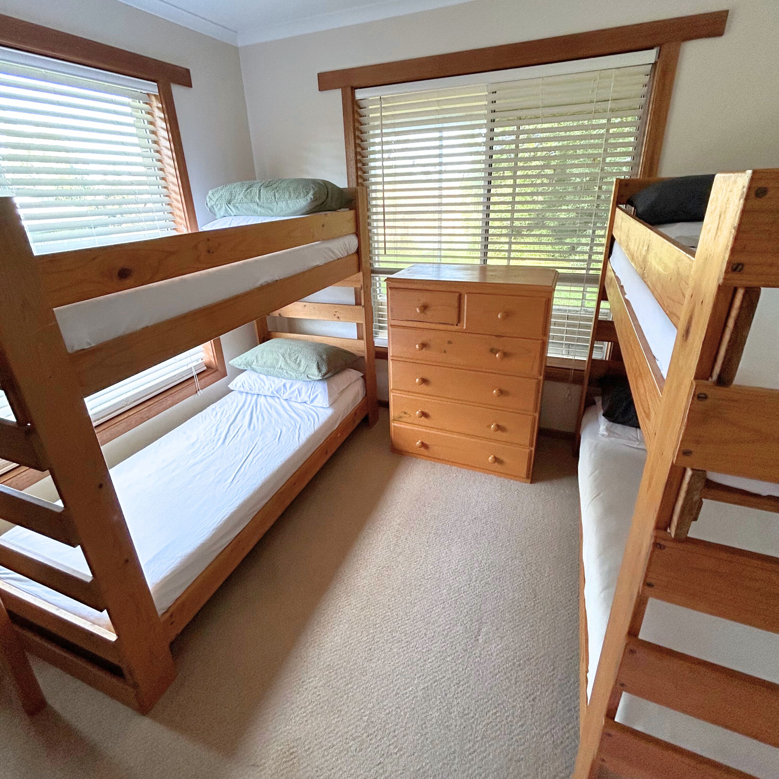 A bunk bed room with a wooden dresser and a window with blinds.