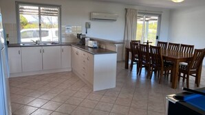 Una cocina con armarios blancos, una isla central y un comedor con sillas de madera.
