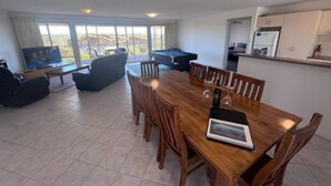 Amplia sala de estar con mesa de comedor de madera, asientos cómodos, un ventanal con vistas y una kitchenette.