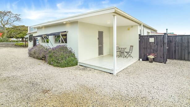 Une maison moderne dotée d’un patio couvert, d’une cour clôturée et d’une allée gravillonnée.