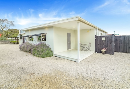 A modern house with a covered patio, a fenced yard, and a gravel driveway.