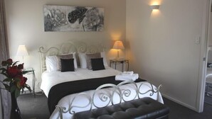 Une chambre d’hôtel bien aménagée, avec un lit, deux lampes de chevet, un élément décoratif mural et une petite table sur laquelle est posé un vase de fleurs.