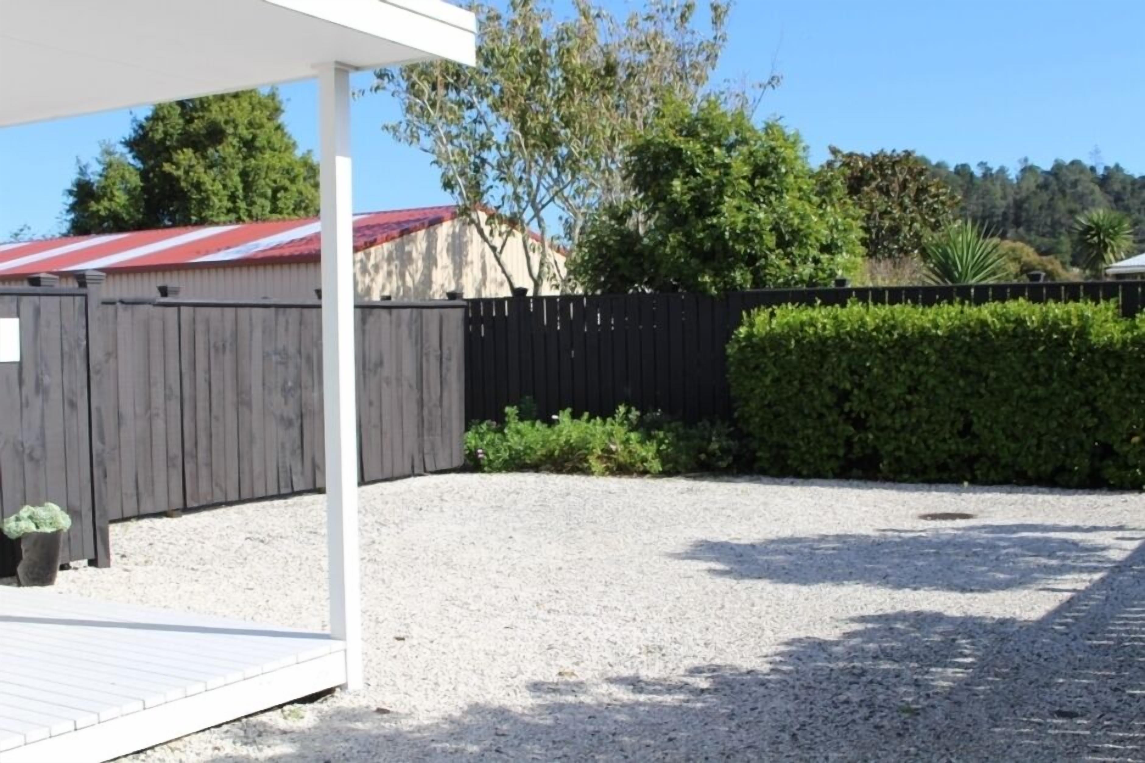 A covered outdoor area with a gravel surface, a wooden fence, and a hedge.