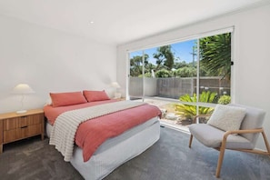 A bedroom with a bed, bedside tables, a chair, and a large sliding glass door to a balcony.