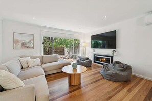 A modern living room with a sofa, a round coffee table, a fireplace, and a television.