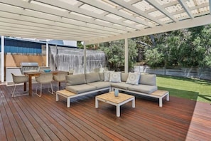An outdoor patio with a wooden deck, a built-in grill, a sofa with cushions, and a small table.