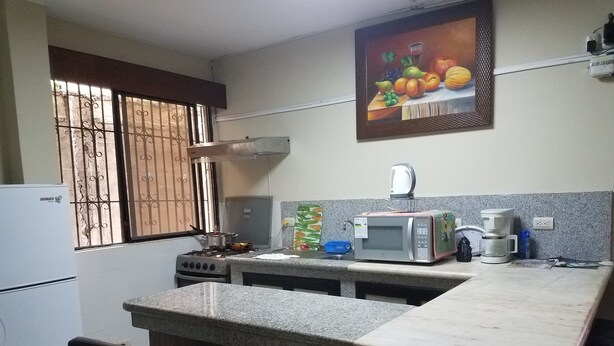 A kitchen with a gas stove, a microwave, a refrigerator, and a window with bars. - HOLA SOY SERENA, MI PROPIEDAD  SE LLAMA  "CASA SERENA" (GUAYAQUIL)