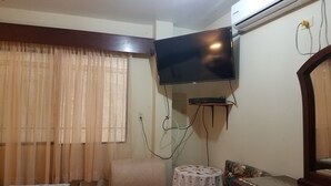 A hotel room with a bed, a chair, a small table with a floral tablecloth, a flat-screen TV mounted on the wall, and an air conditioning unit. - HOLA SOY SERENA, MI PROPIEDAD  SE LLAMA  "CASA SERENA" (GUAYAQUIL)