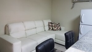 A small, clean room with a white sofa, a patterned pillow, two black chairs, and a white refrigerator. - HOLA SOY SERENA, MI PROPIEDAD  SE LLAMA  "CASA SERENA" (GUAYAQUIL)