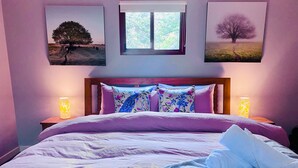 A bedroom with a bed, two bedside lamps, and three framed pictures on the wall.