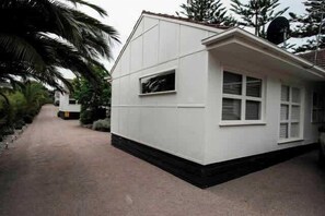 A single-story house with a flat roof, a front porch, and a driveway leading to a parked vehicle. - Portsea Haven (Portsea)