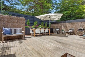 An outdoor patio with a wooden deck, a dining table with chairs, a bench, and an umbrella.