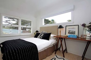 A bedroom with a bed, bedside table, lamp, framed picture, and window with blinds.