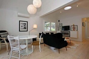 A modern living room with a white dining table, black sofa, and a TV on a white stand. - Portsea Haven (Portsea)