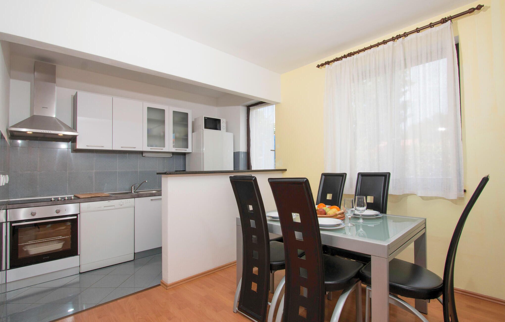 A modern kitchen with white cabinets, a stainless steel stove, and a dining area with a glass table and four chairs.