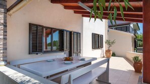 Ein Außenbereich zum Essen mit einem weißen Tisch und Bänken, einer Pergola darüber und Blumentöpfen.