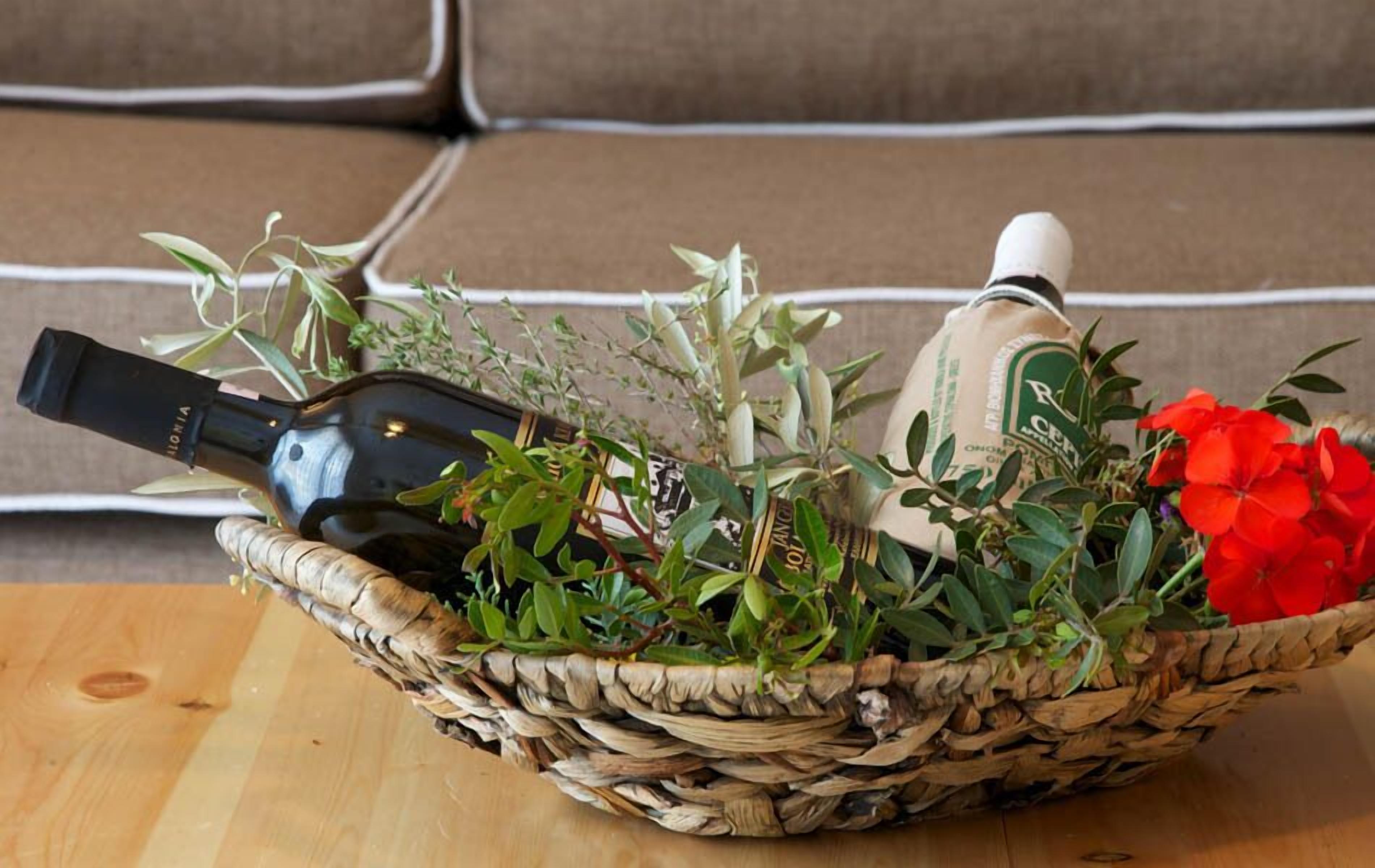 A wicker basket containing a bottle, a plant, and a red flower on a wooden surface.