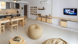 A modern kitchen with wooden cabinets, a dining table with chairs, a large bean bag chair, and a flat-screen TV mounted on the wall. - G Living 365 (Kefalonia)