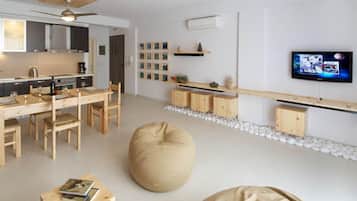 Eine moderne Küche mit Holzausstattung, einem Esstisch mit Stühlen, einem großen Sitzsack und einem flachbildfernseher an der Wand.