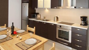A modern kitchen with dark cabinetry, a stainless steel refrigerator, a microwave, a coffee maker, and an oven. - G Living 365 (Kefalonia)