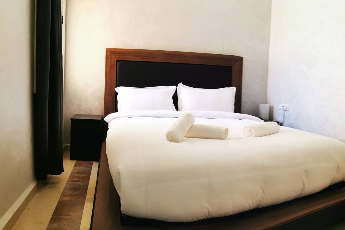 A neatly made bed with white linens and a wooden headboard in a hotel room.