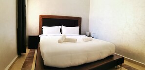 A neatly made bed with white linens and a wooden headboard in a hotel room. - Amwaj Hotel (El Jadida)