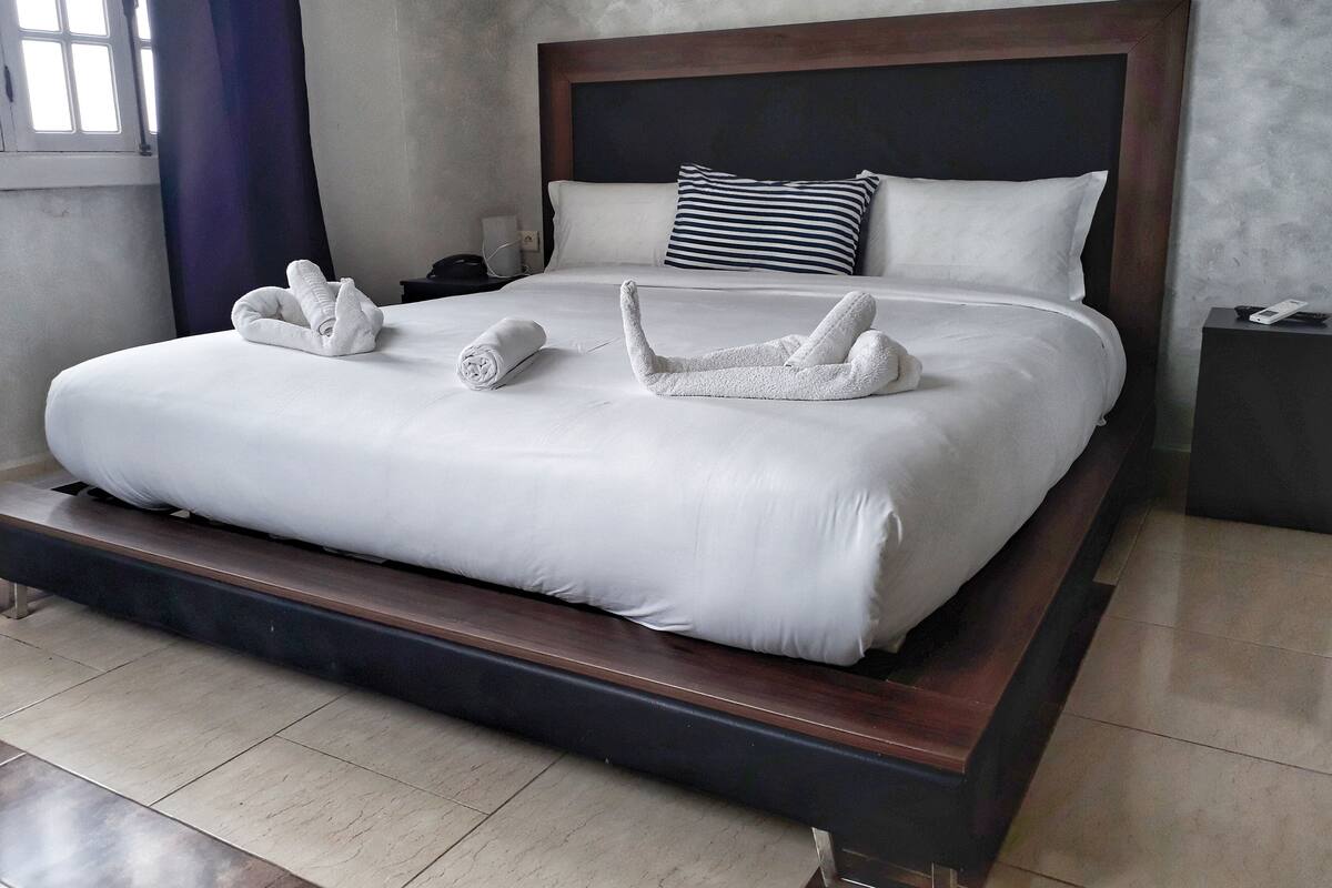A neatly made bed with white linens and towels arranged in a swan shape.