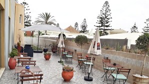 An outdoor patio with multiple tables and chairs, potted plants, and umbrellas. - Amwaj Hotel (El Jadida)