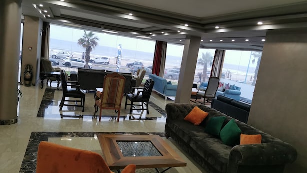 A hotel lobby with a seating area, a coffee table, and a view of the beach and cars outside. - Amwaj Hotel (El Jadida)