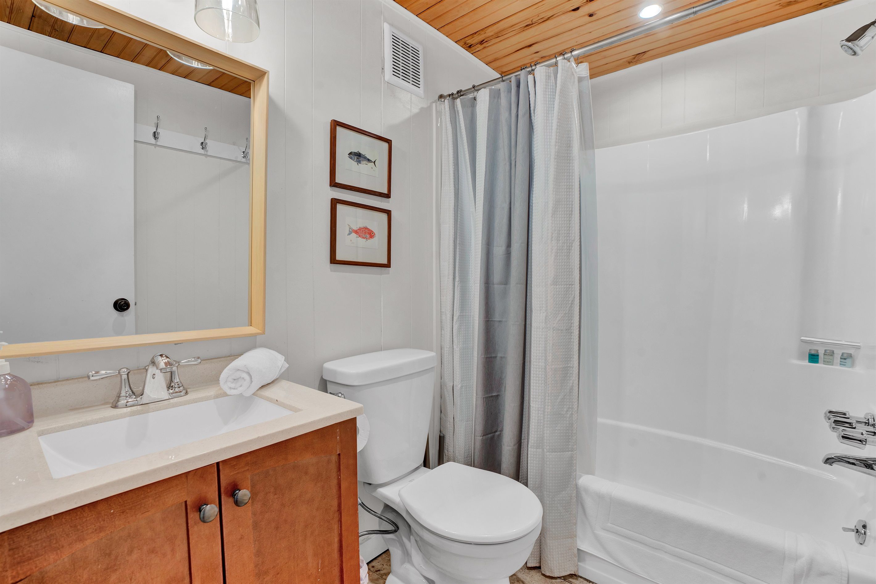 A bathroom with a wooden vanity, a toilet, a shower with a curtain, and two framed pictures on the wall.