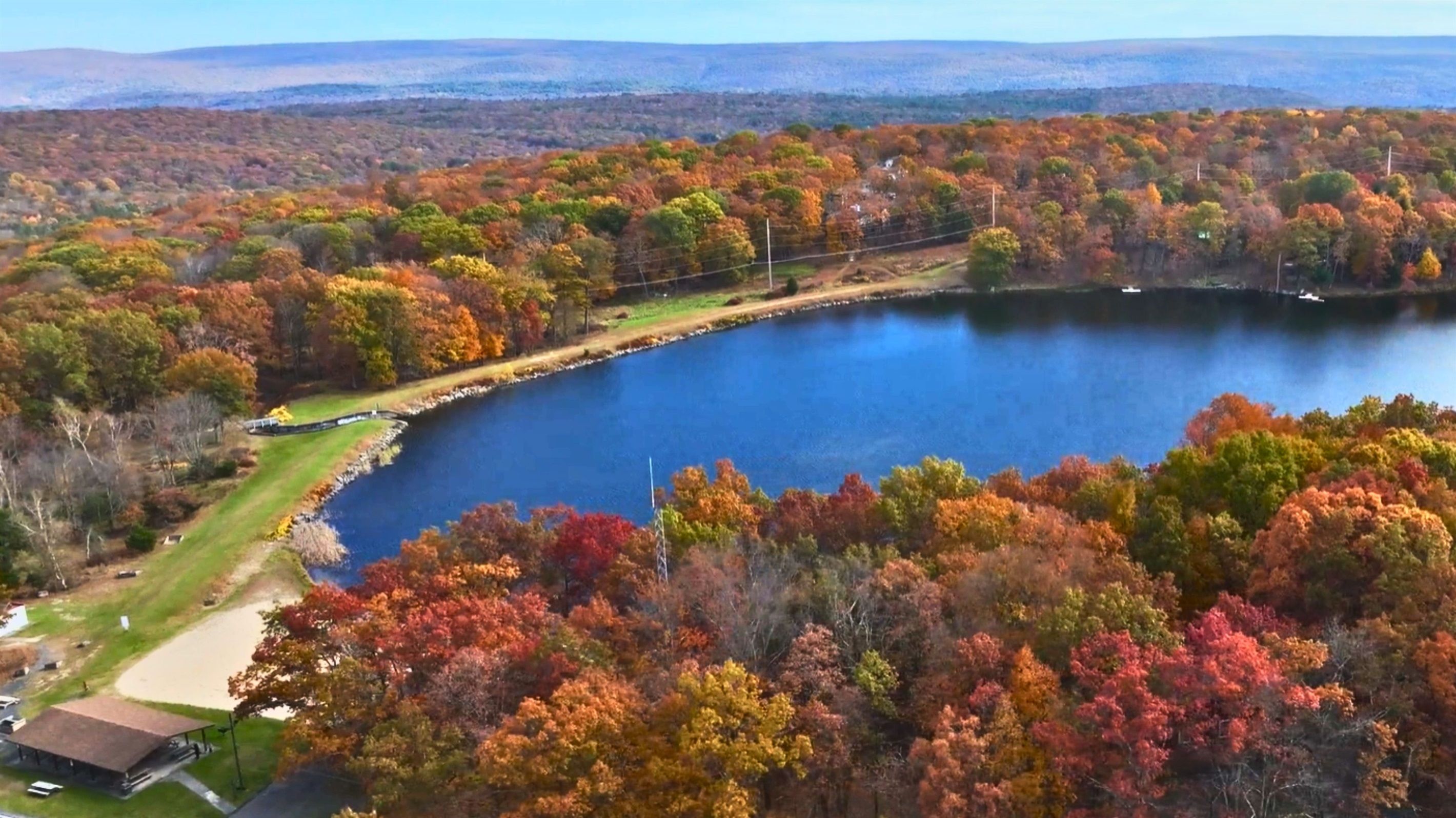 A lake surrounded by trees with autumn foliage, a dock, and a small building.